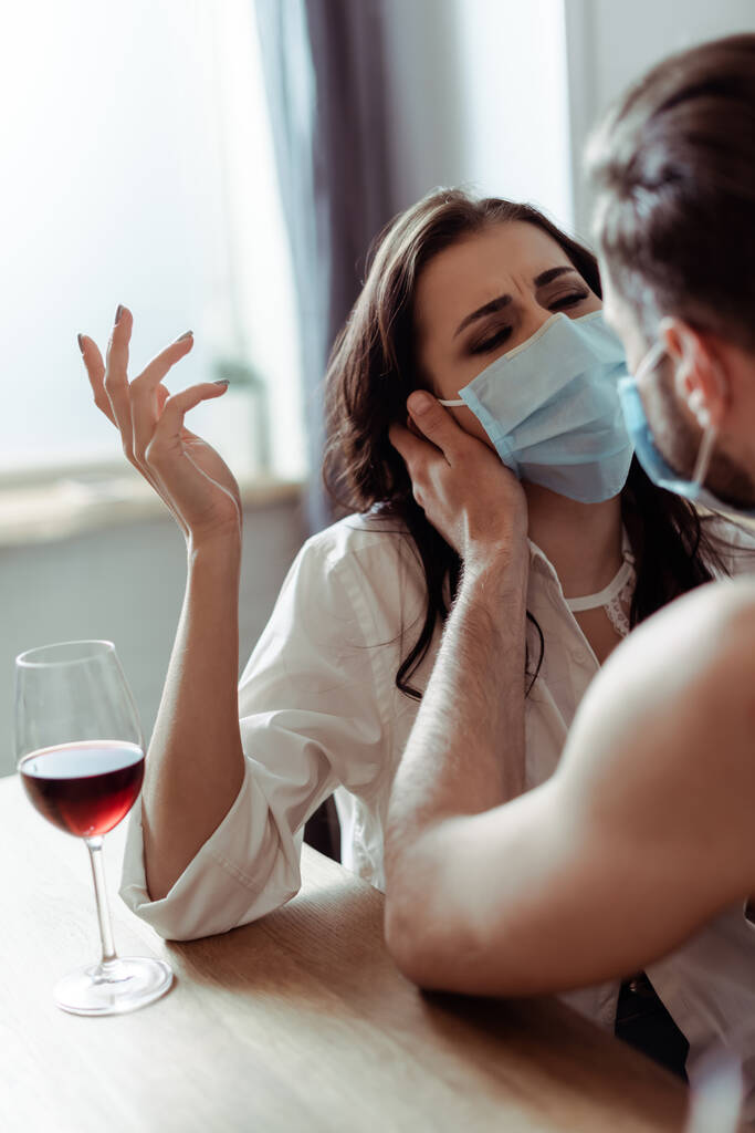 Mann mit junger unzufriedener Frau in medizinischer Maske am Tisch - Foto, Bild
