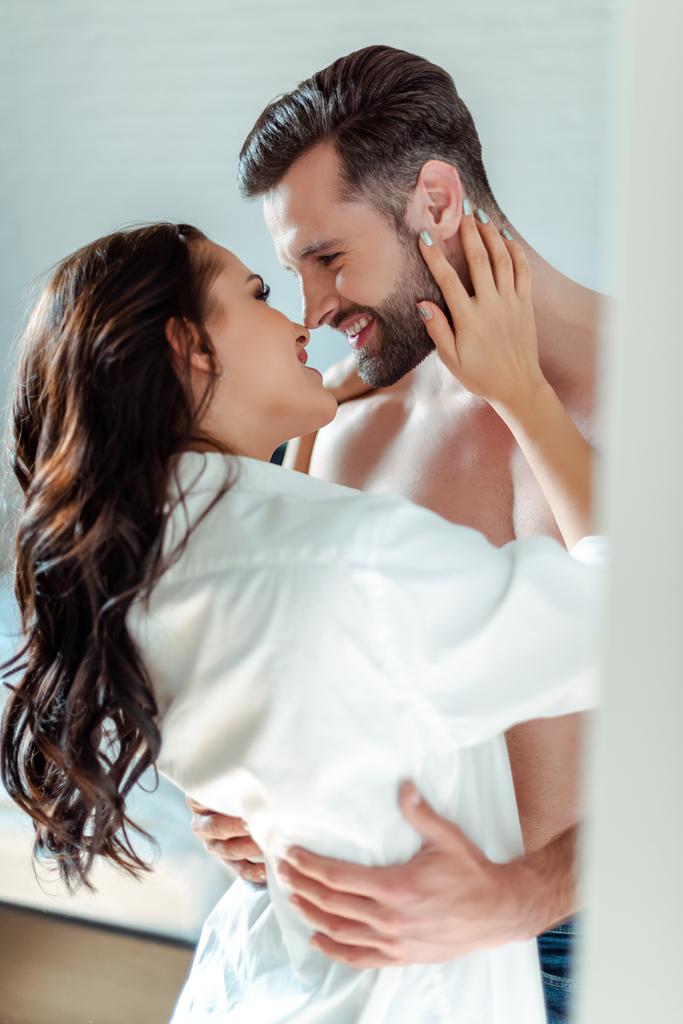 selective focus of smiling sexy young brunette woman in shirt hugging man with bare torso - Photo, Image