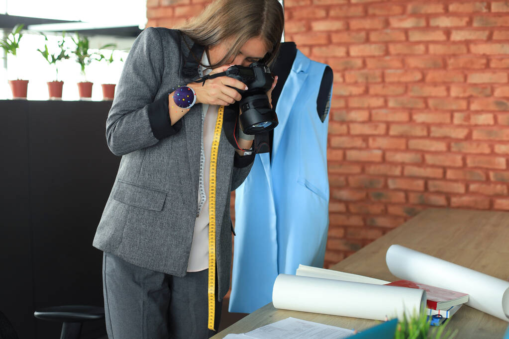 彼女の創造的なオフィスの机の近くに立っている間、デジタルカメラを使用して若いデザイナーを集中 - 写真・画像