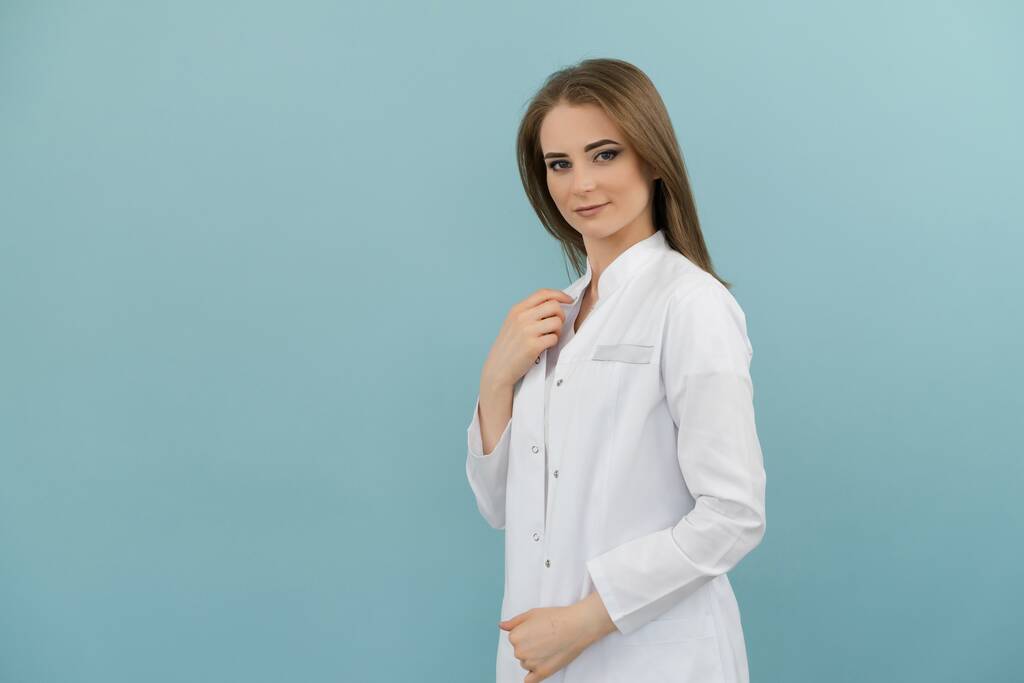 Позитивная женщина-врач в пальто на синем фоне
 - Фото, изображение