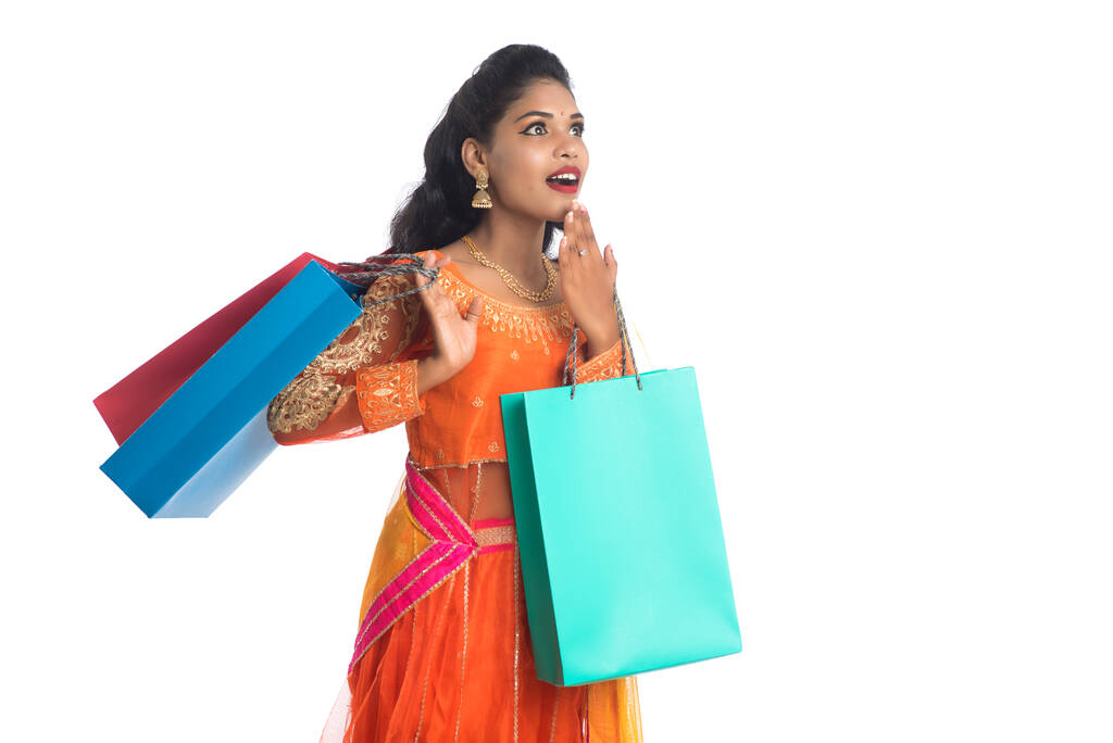 Piękna indyjska młoda dziewczyna trzyma torby na zakupy nosząc tradycyjne ubrania etniczne. Izolacja na białym tle - Zdjęcie, obraz