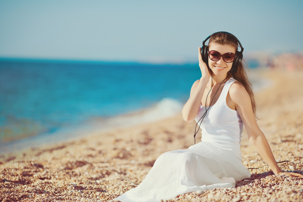 zenehallgatás fejhallgató, a tengerparton kék ég ellen, a gyönyörű nő - Fotó, kép