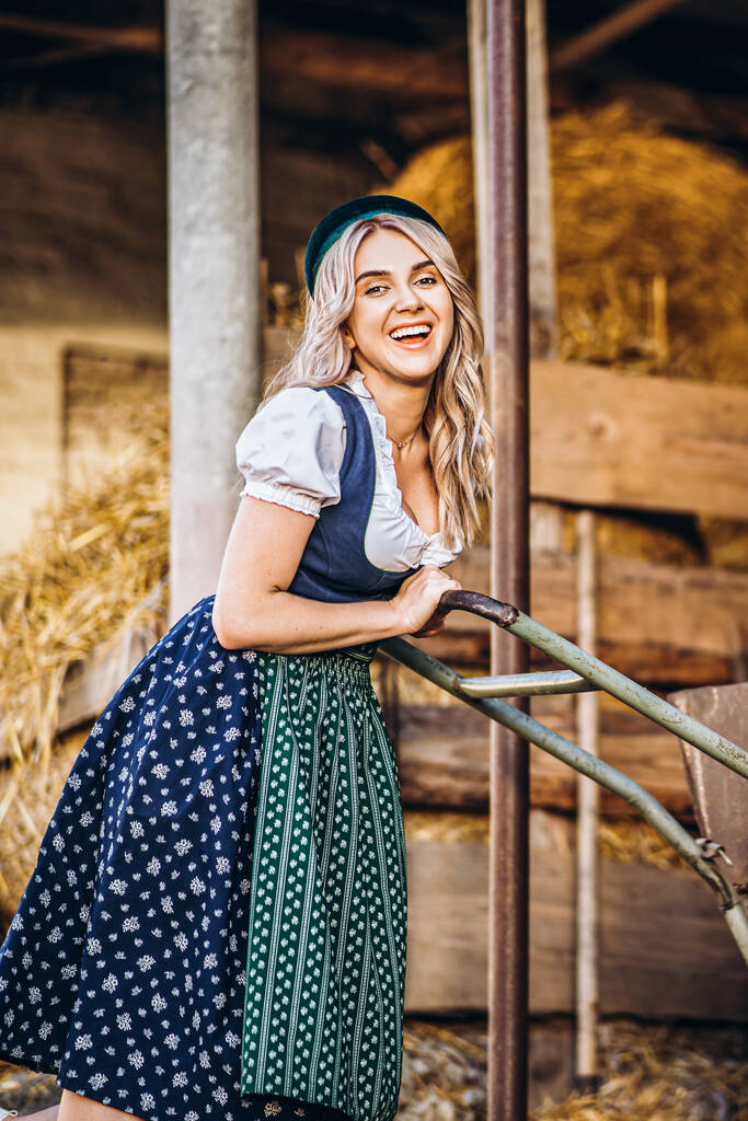 Pěkně usměvavá blondýna v tradičních šatech s kolečkem pracuje na dvorku farmy  - Fotografie, Obrázek