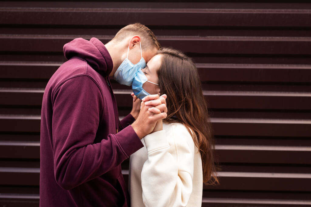 Pareja en cuarentena tratando de besarse usando una máscara al aire libre. Concéntrate en las manos
 - Foto, imagen