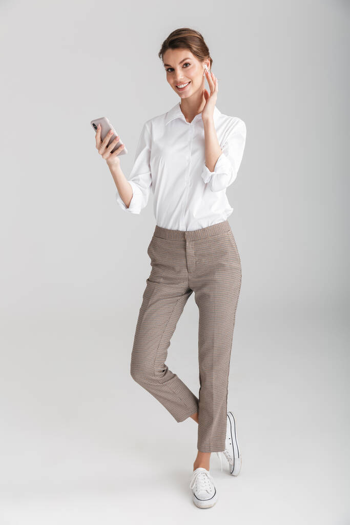 Зображення усміхненої красивої жінки з використанням бездротових навушників та мобільного телефону ізольовано на білому тлі
 - Фото, зображення