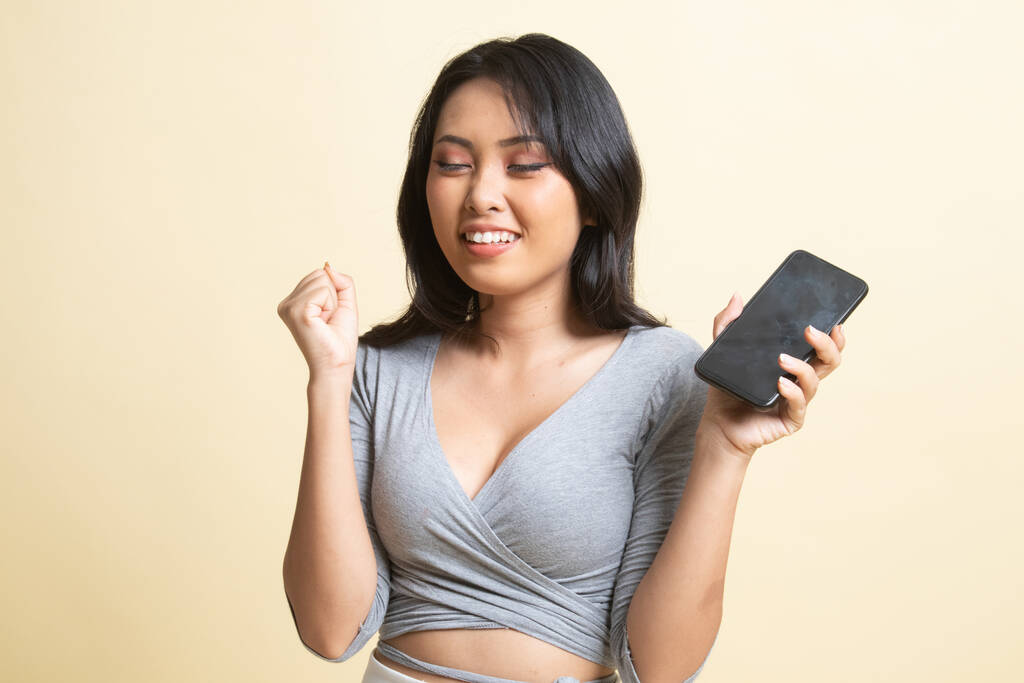Jovem mulher asiática feliz com telefone móvel no fundo bege
 - Foto, Imagem