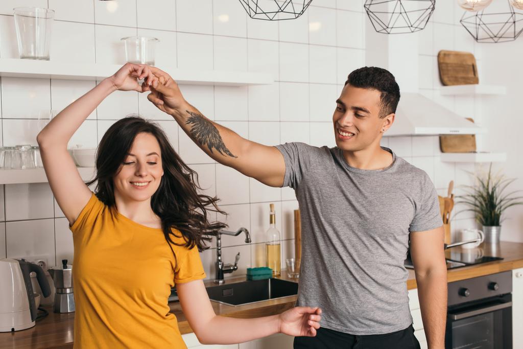 alegre interracial casal sorrindo enquanto dança na cozinha
  - Foto, Imagem
