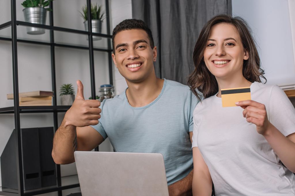 happy girl holding credit card and mixed race boyfriend showing thumb up near laptop  - Photo, Image