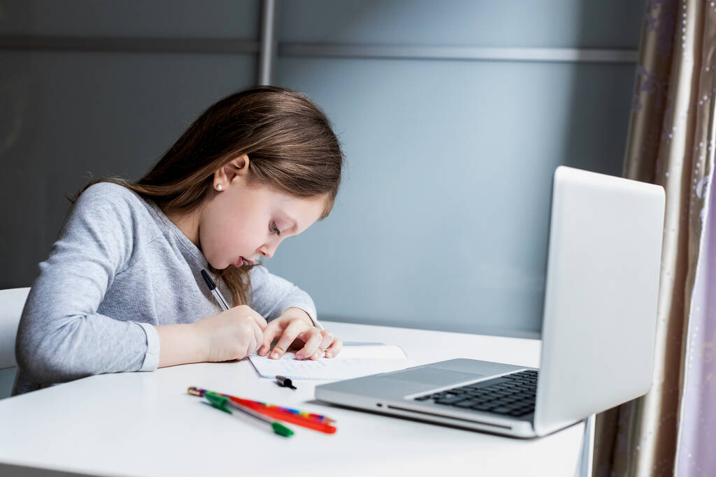 Kleuterschoolmeisje met behulp van gadgets om te studeren. Peuter meisje doet haar huiswerk met laptop thuis. Onderwijs en afstandsonderwijs voor kinderen. Thuisonderwijs tijdens de quarantaine. Blijf thuis entertainment - Foto, afbeelding