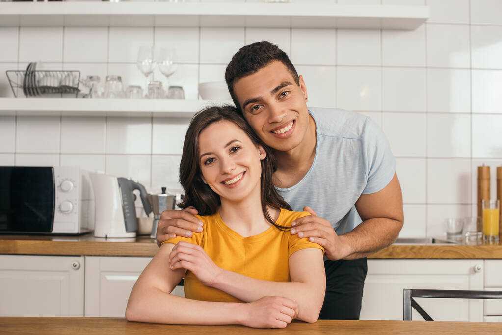 весёлый смешанный расовый мужчина обнимает привлекательную девушку на кухне
 - Фото, изображение