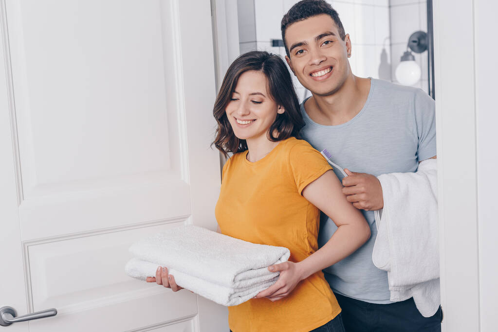 positive multiracial couple holding towels in bathroom  - Photo, Image