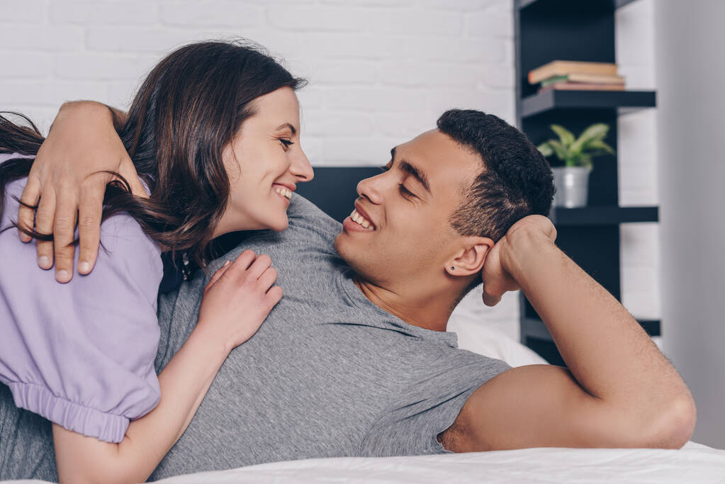 guapo bi-racial hombre acostado en la cama y abrazando atractiva chica
  - Foto, Imagen