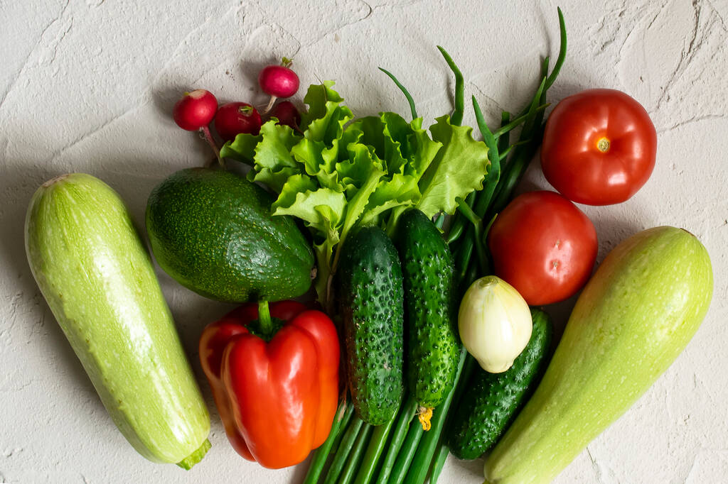 Friss zöld, vörös, bio zöldségek választéka. cukkini, uborka, hagyma, avokádó, saláta, bors, paradicsom és retek konkrét alapon. lapos fektetés - Fotó, kép
