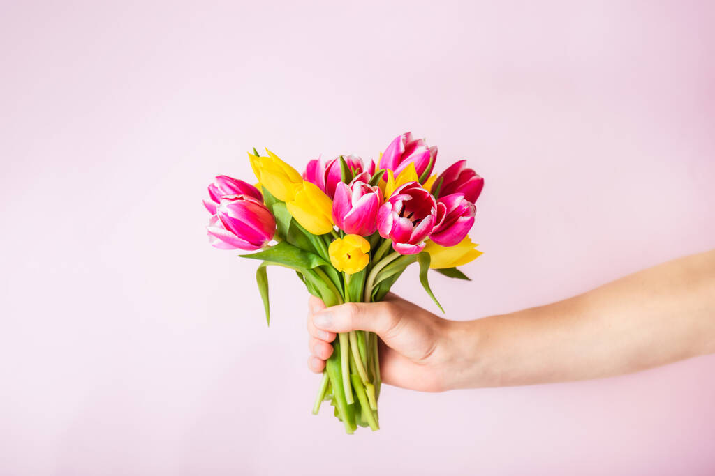 淡いピンクの背景に美しいピンクと黄色のチューリップの花束を保持男性の手。グリーティングカードのモックアップ。誕生日、母親と女性の日。選択的フォーカス。スペースのコピー. - 写真・画像