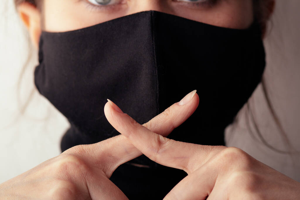 jovem mulher em uma máscara protetora preta mostrando um gesto de silêncio com dois dedos cruzados na boca, conceito de silêncio da verdade, privacidade da informação, conspiração, traição da informação
 - Foto, Imagem