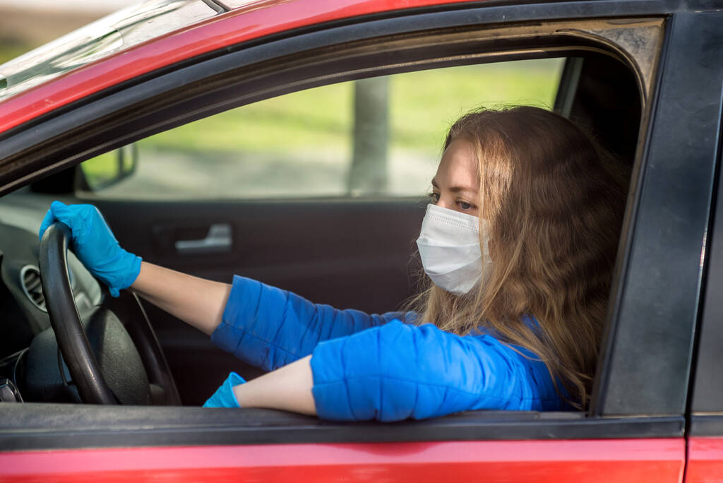 Kobieta prowadząca samochód w ochronnej masce medycznej i rękawiczkach. Styl życia i bezpieczna jazda podczas pandemii koronawirusa w czasie kwarantanny. Chronić kierowcę i pasażerów. Nowa normalna i nowoczesna rzeczywistość - Zdjęcie, obraz