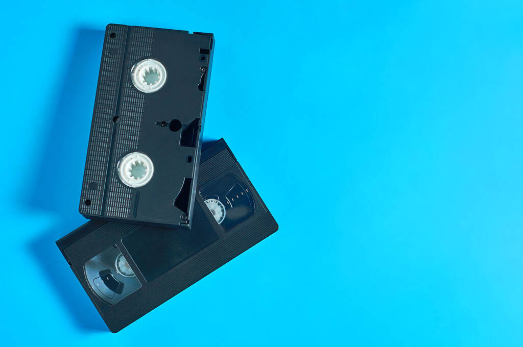 青い机の上に黒い古いプラスチック製のvhビデオカセットが2つあります。90年代のコンセプト。コピースペース。平敷 - 写真・画像
