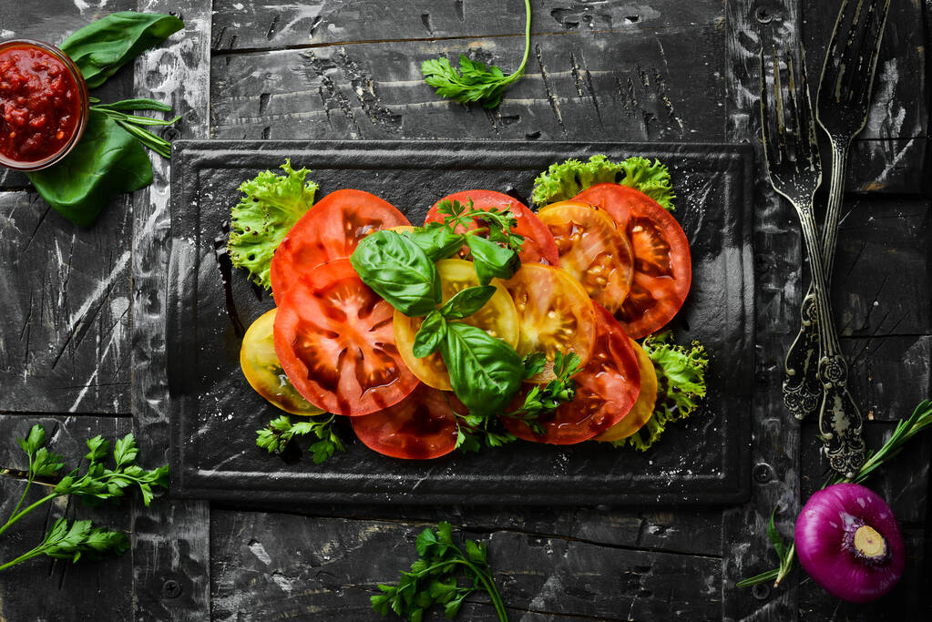 Salad of fresh tomatoes and basil on a black stone plate. Top view. Free copy space. - Photo, Image