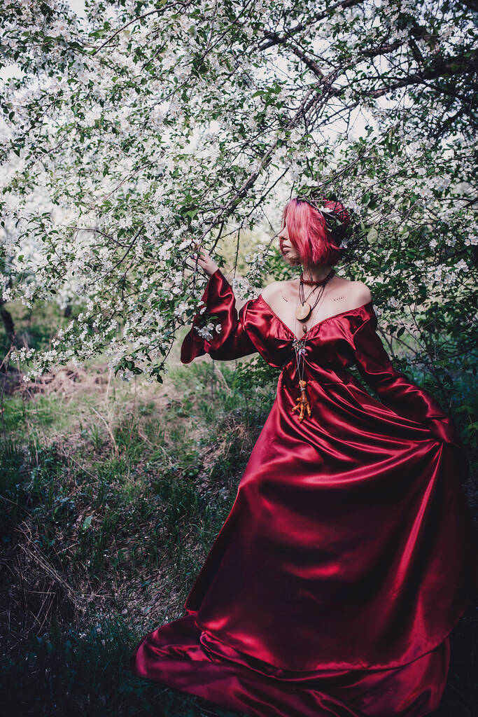 Menina de cabelo vermelho e vermelho na forma de um druida em árvores de maçã
 - Foto, Imagem