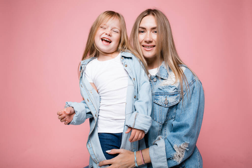 Familie portret van een jonge moeder en dochter in denim jassen met blond lang haar en glimlachend op de foto. - Foto, afbeelding