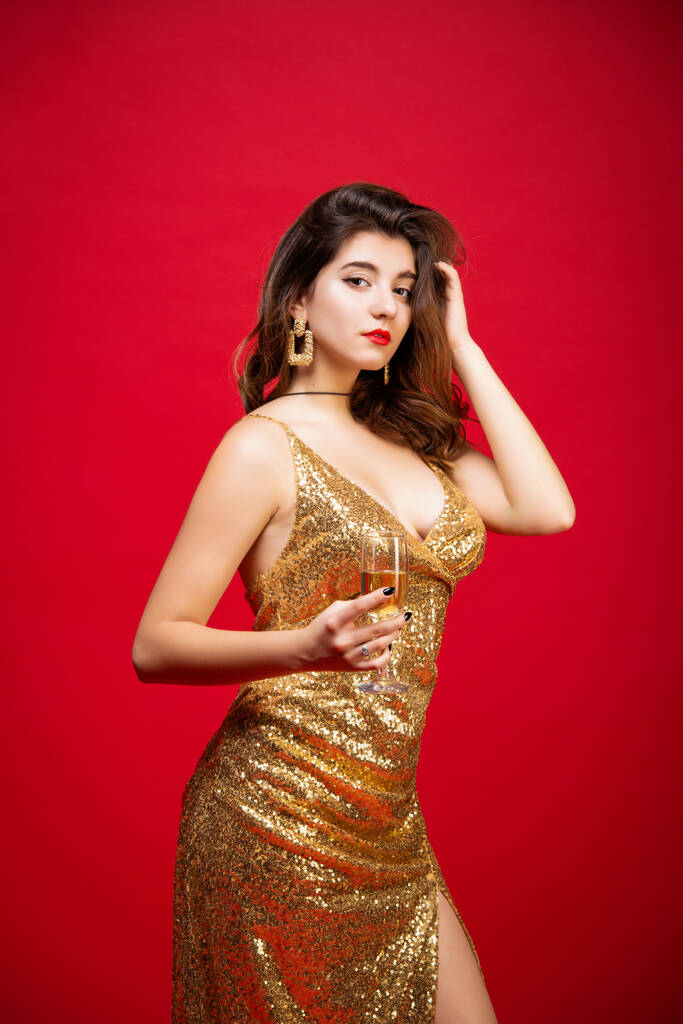Mulher sexy em vestido de ouro com batom vermelho e com champanhe na mão sobre fundo vermelho feriado. Conceito de um feriado de Ano Novo, festa de aniversário
. - Foto, Imagem