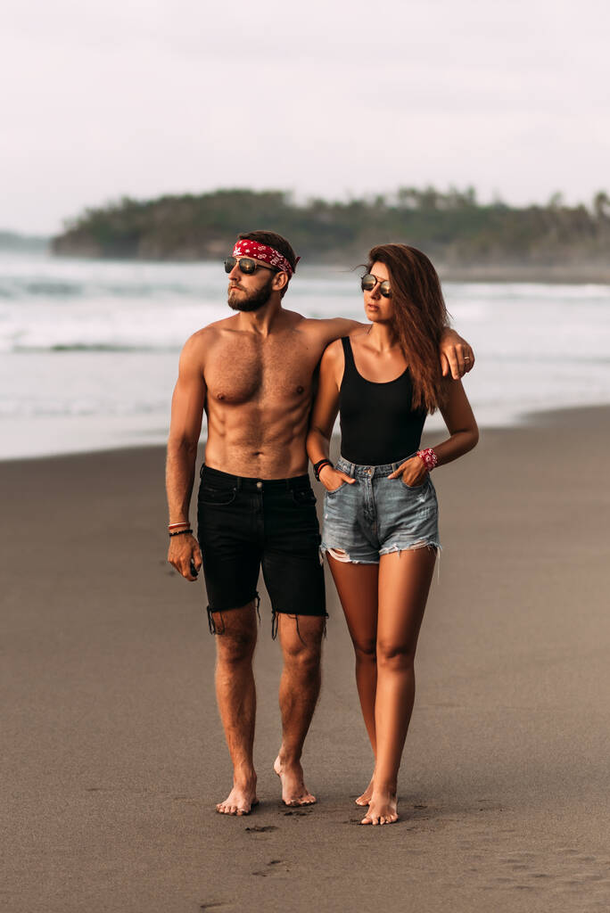 Szczęśliwa para spacerująca po piaszczystej plaży. Para zakochana o zachodzie słońca nad morzem. Wakacje na wyspie Bali. Romantyczna para ciesząca się spacerem po plaży o zachodzie słońca. Kochankowie na wybrzeżu. Podróż poślubna - Zdjęcie, obraz