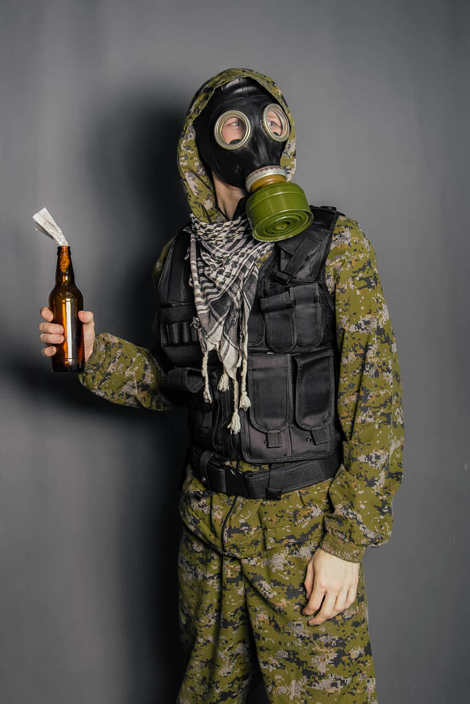 テロの概念は、迷彩服、ボディアーマーとガスマスクに抗議し、 Molotovカクテル、お香の混合物をスローします。灰色の背景のスタジオ写真. - 写真・画像