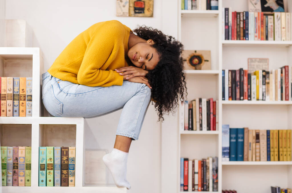 Imagen de una joven afroamericana durmiendo sentada en un estante en la sala de estar
 - Foto, Imagen