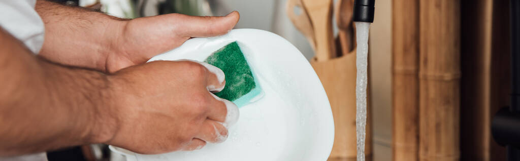 panoramatický záběr muže držícího houbu při mytí bílého talíře  - Fotografie, Obrázek