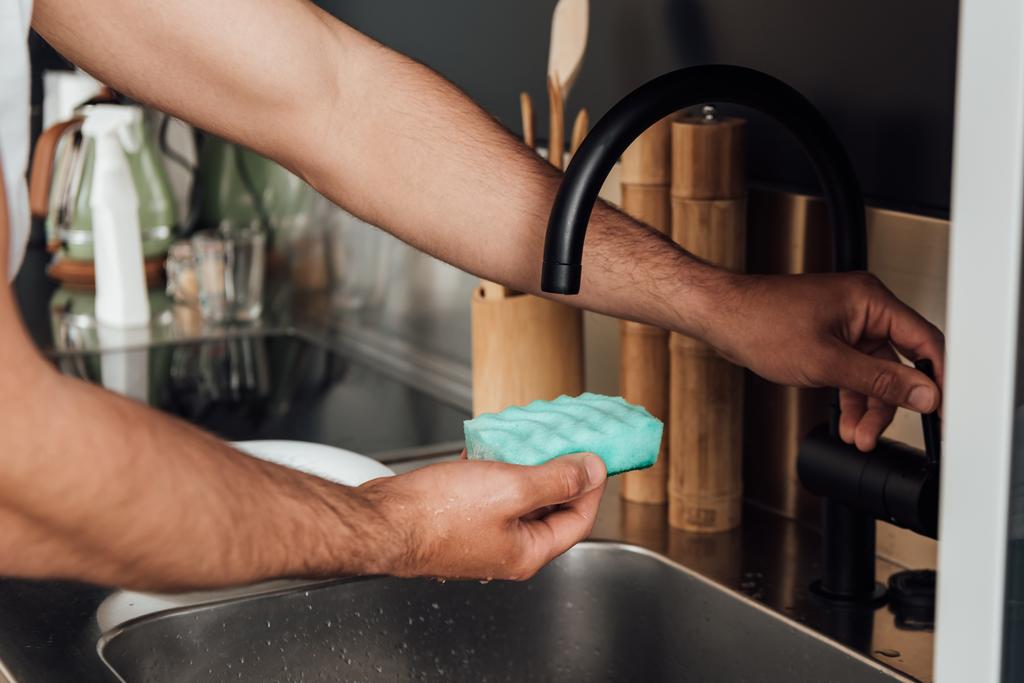 vista ritagliata dell'uomo che tiene la spugna vicino al rubinetto in cucina
  - Foto, immagini