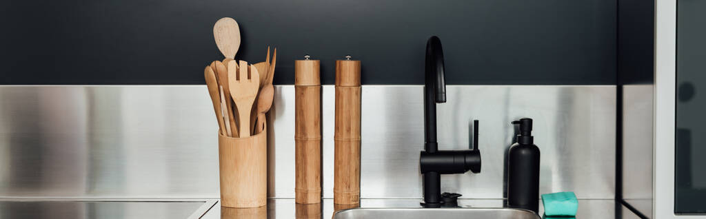 panoramisch concept van houten pepermolen en zoutmolen bij kraan, gootsteen, zeepdispenser en spons in de keuken  - Foto, afbeelding