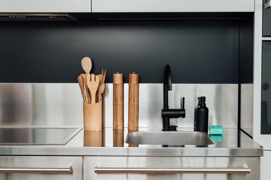 drewniany młyn pieprzowy i młyn solny w pobliżu kran, zlewozmywak, dozownik mydła i gąbka w kuchni  - Zdjęcie, obraz