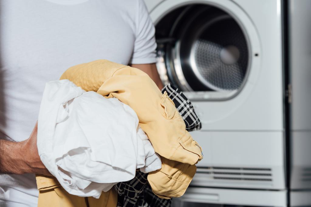 Kirli çamaşırları beyaz çamaşır makinesinin yanında tutan adamın görüntüsü.  - Fotoğraf, Görsel