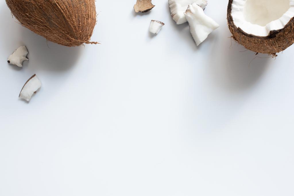 vrchní pohled na celé a popraskané chutné kokosové půlky a kousky na bílém pozadí - Fotografie, Obrázek