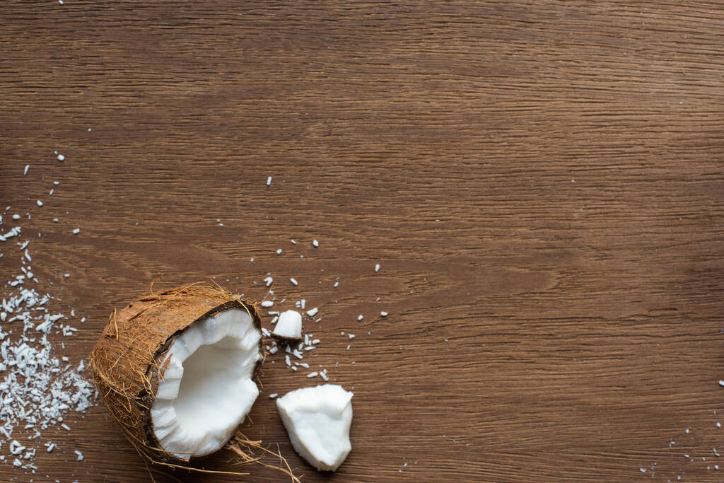 vrchní pohled na čerstvé chutné kokosové půlky v blízkosti vloček na dřevěném stole - Fotografie, Obrázek