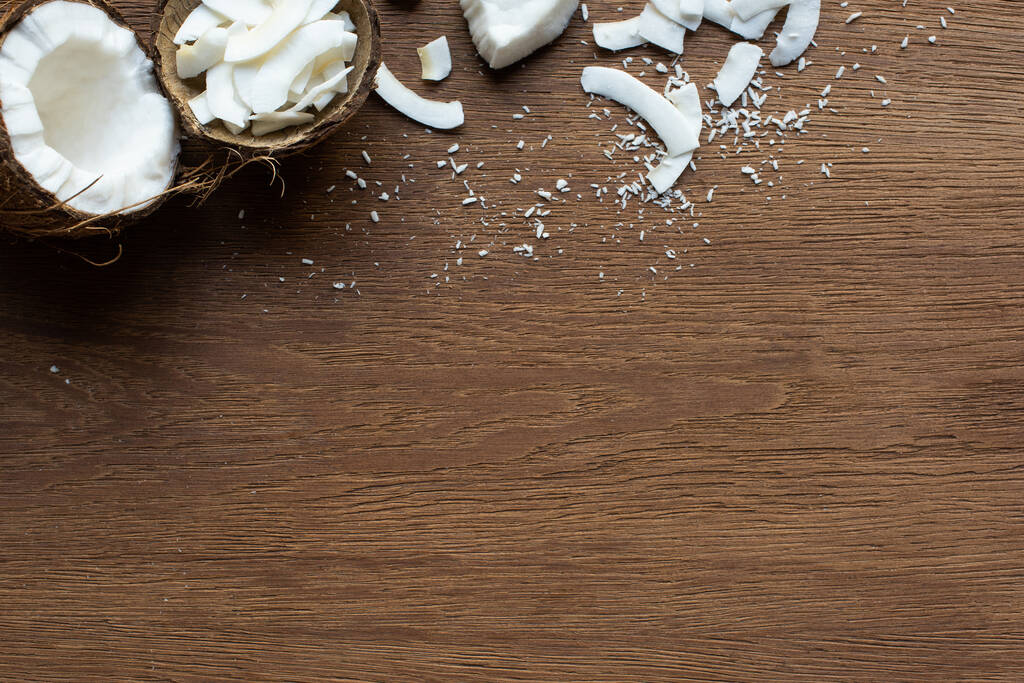 vrchní pohled na čerstvé chutné kokosové půlky v blízkosti vloček ve skořápce na dřevěném stole - Fotografie, Obrázek