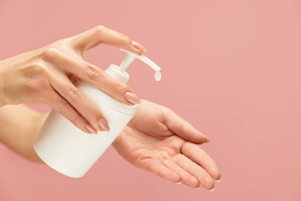 Kézhigiénia. Folyékony szappan palack női kézben rózsaszín háttér ellen. Napi személyi higiéniai rutin a vírusmegelőzés. Mosd meg a kezed, mert egészséges vagy..  - Fotó, kép