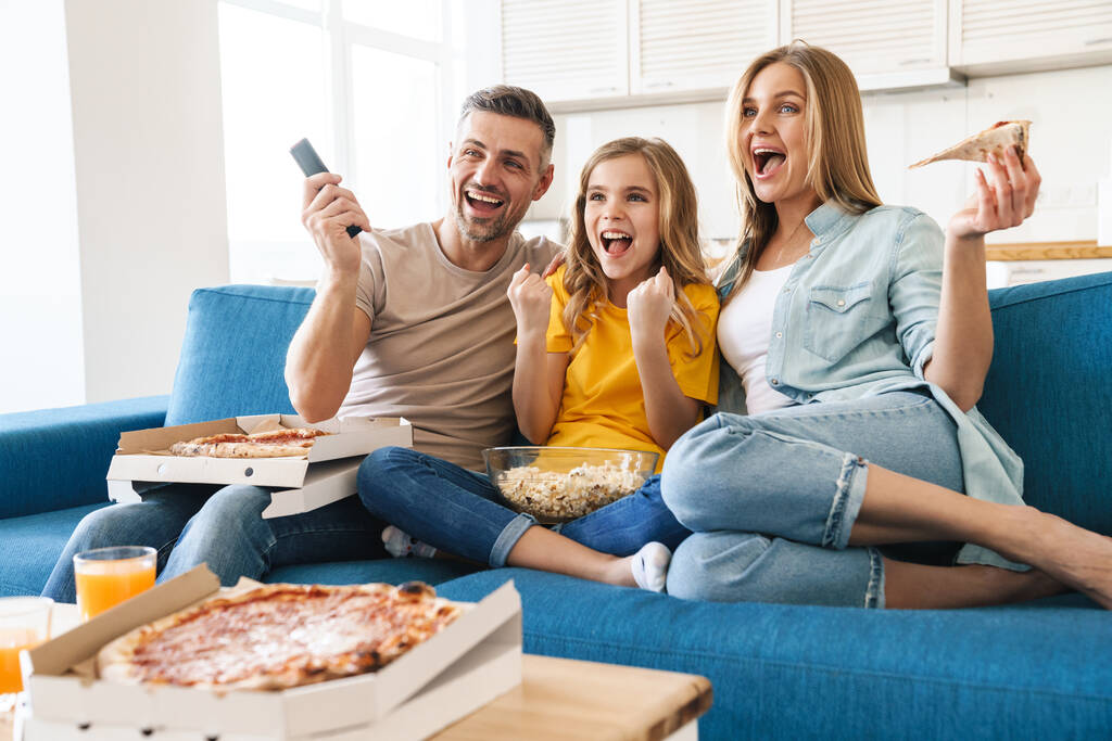 Фото збудженої красивої кавказької сім'ї, що їсть попкорн та піцу під час перегляду телевізора вдома
 - Фото, зображення