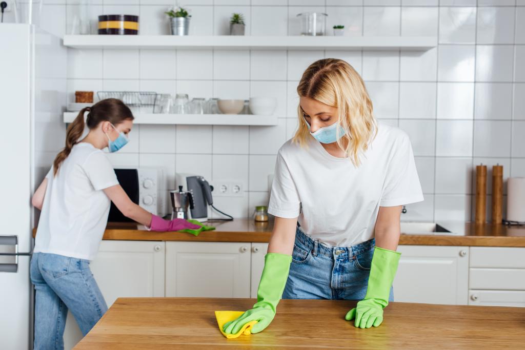 selectieve focus van de vrouw in medisch masker en zus doen huishoudelijk werk  - Foto, afbeelding