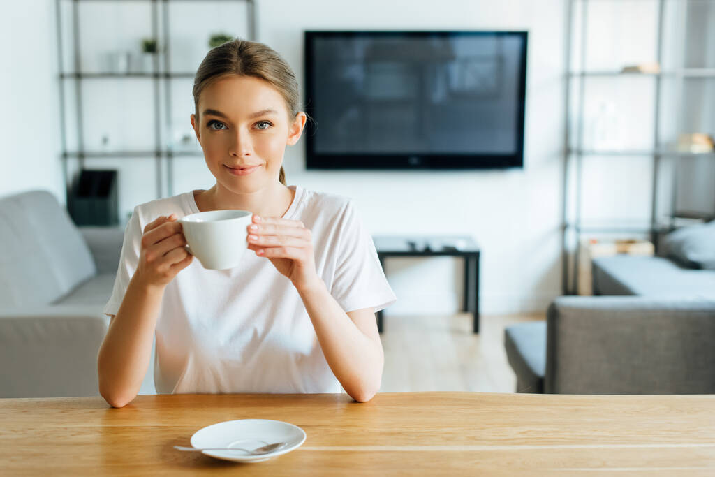 mujer feliz mirando a la cámara y sosteniendo la taza de café
 - Foto, Imagen