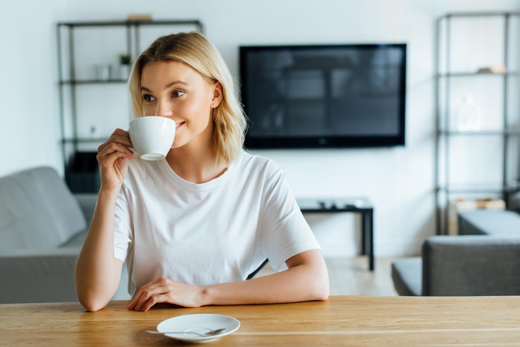 χαρούμενη και ελκυστική γυναίκα πίνοντας καφέ στο σπίτι  - Φωτογραφία, εικόνα