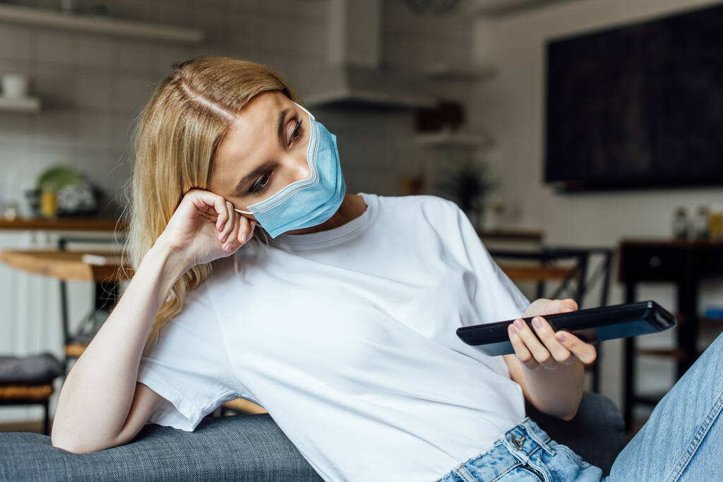 Blondýny dívka v lékařské masky sledování film v obývacím pokoji - Fotografie, Obrázek