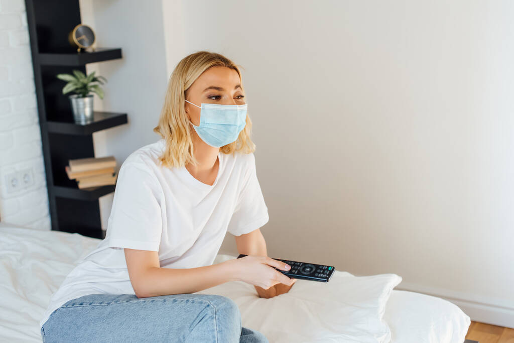 Ragazza bionda in maschera medica con telecomando sul letto
  - Foto, immagini