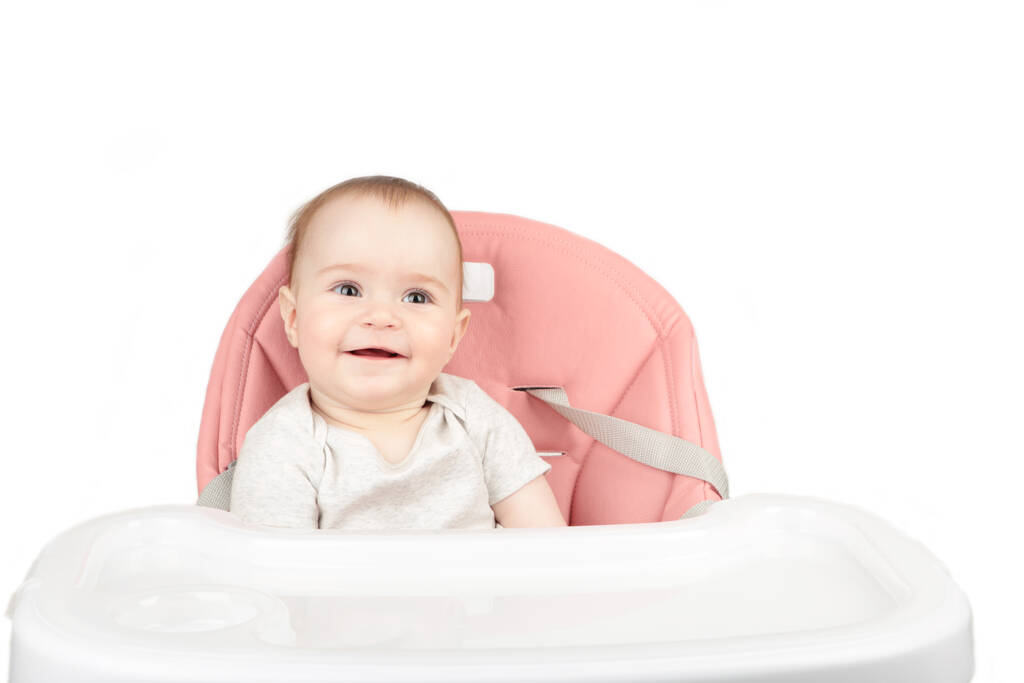 gelukkig baby meisje zitten in een hoge stoel glimlach geïsoleerd op witte achtergrond - Foto, afbeelding