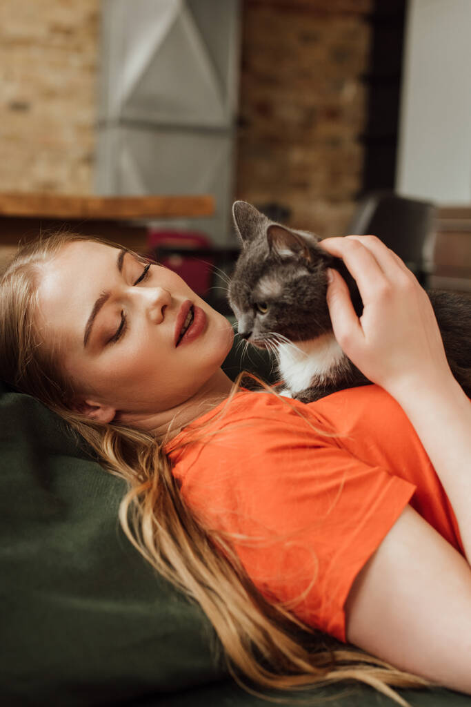aantrekkelijke jonge vrouw op zoek naar schattig kat in woonkamer  - Foto, afbeelding