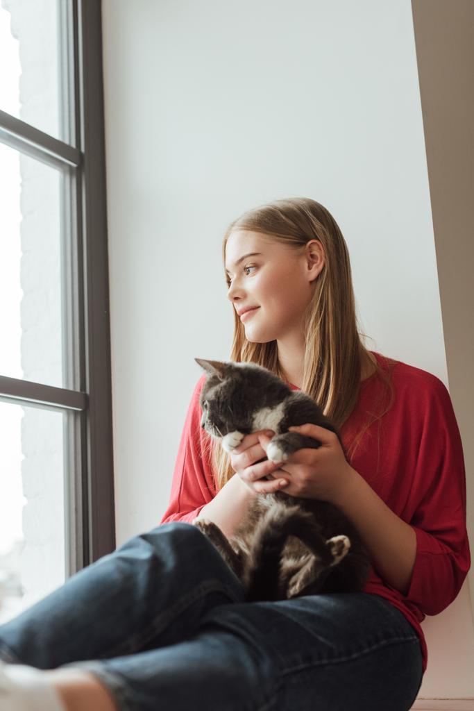 valikoiva painopiste nuori ja onnellinen nainen tilalla söpö kissa istuessaan ikkunalaudalla
  - Valokuva, kuva