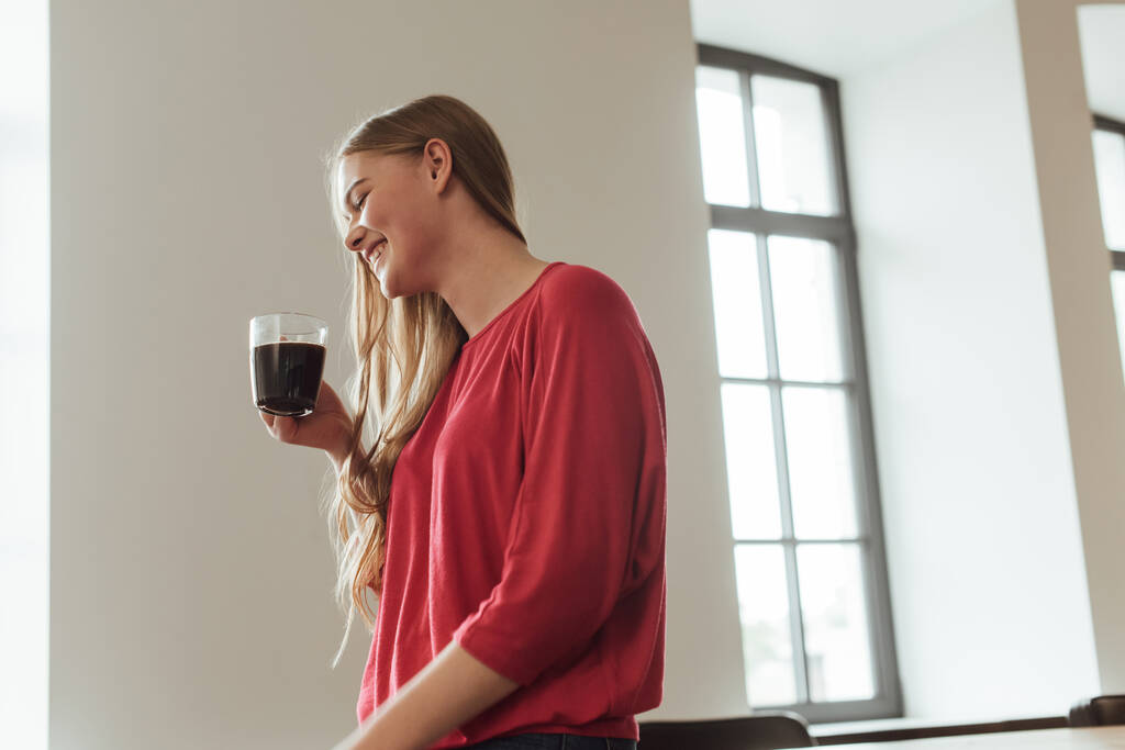 Улыбающаяся женщина держит чашку кофе дома
  - Фото, изображение