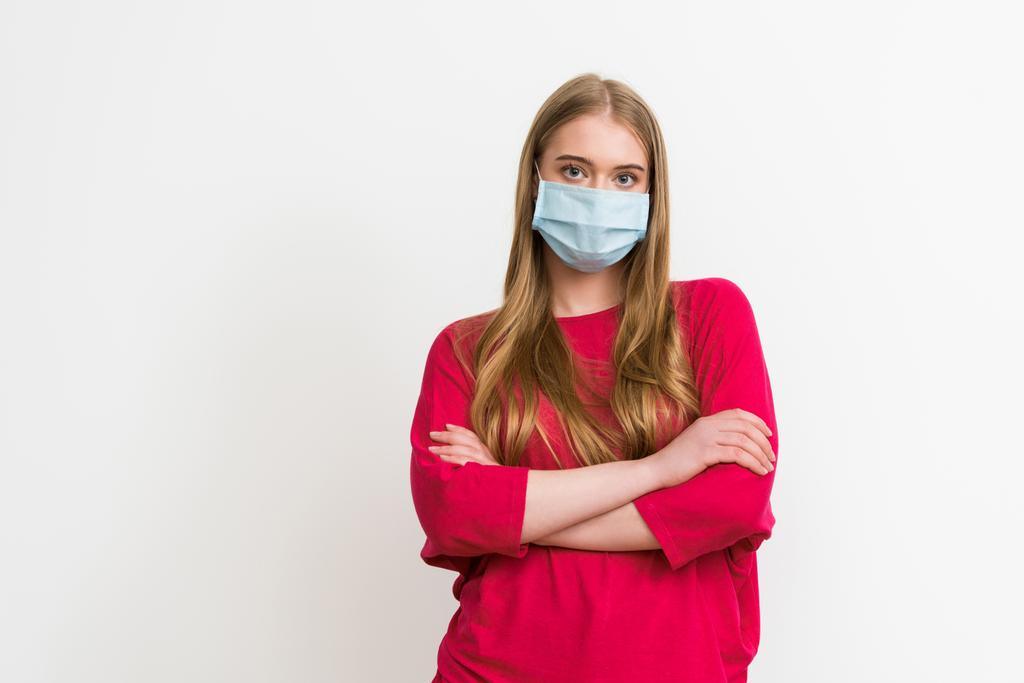 junge Frau in medizinischer Maske steht mit verschränkten Armen isoliert auf weiß  - Foto, Bild