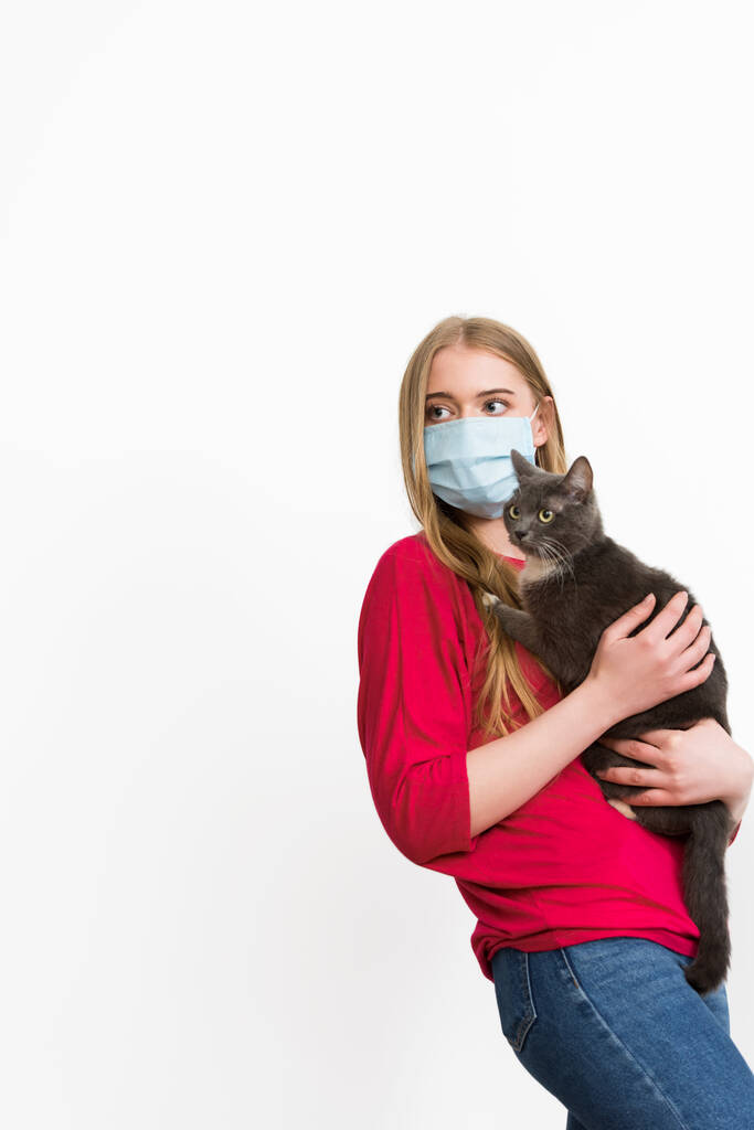 joven mujer en médico máscara celebración en brazos lindo gato aislado en blanco
  - Foto, imagen