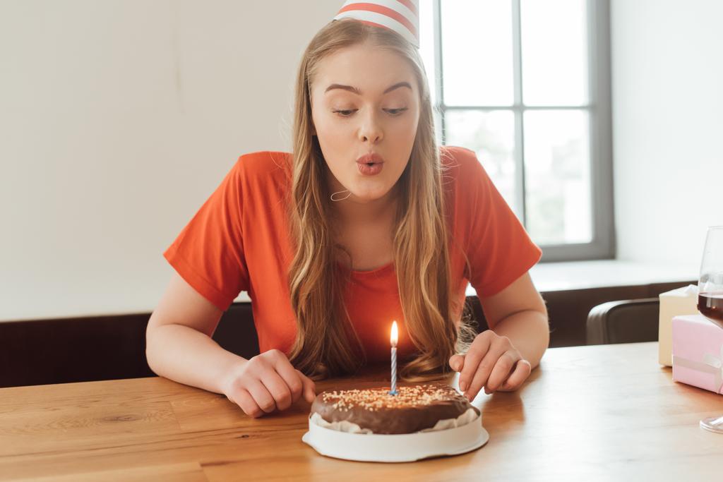молодая женщина задувает свечу на вкусном торте
  - Фото, изображение